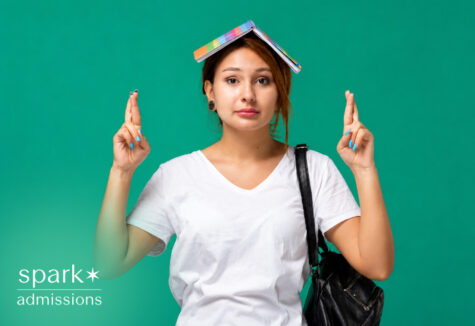 Student crossing fingers with notebook on head hoping for college acceptance