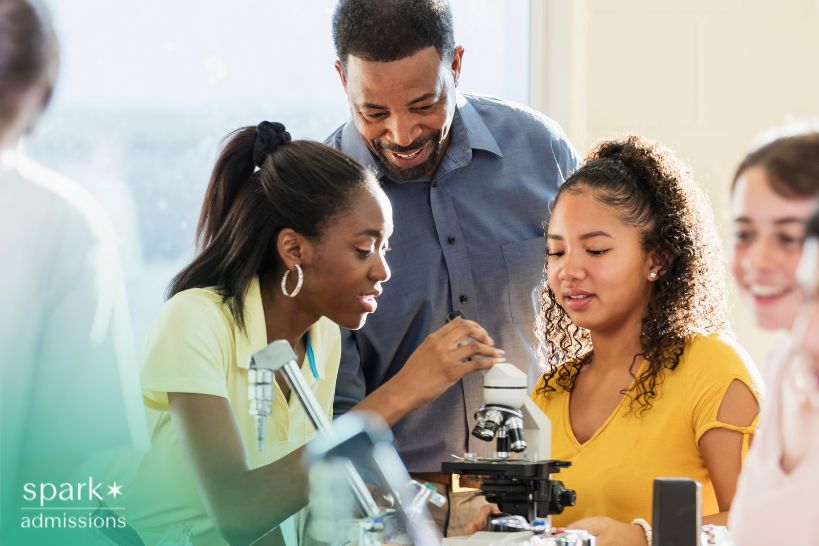 High school students work with a microscope in a science lab while a teacher guides them