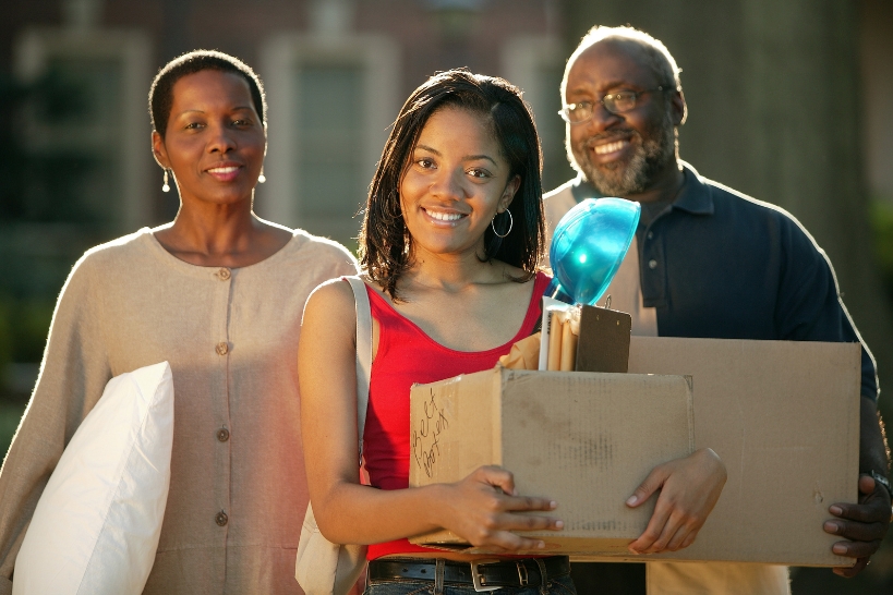 College student carrying moving boxes with her parents during campus move-in day.