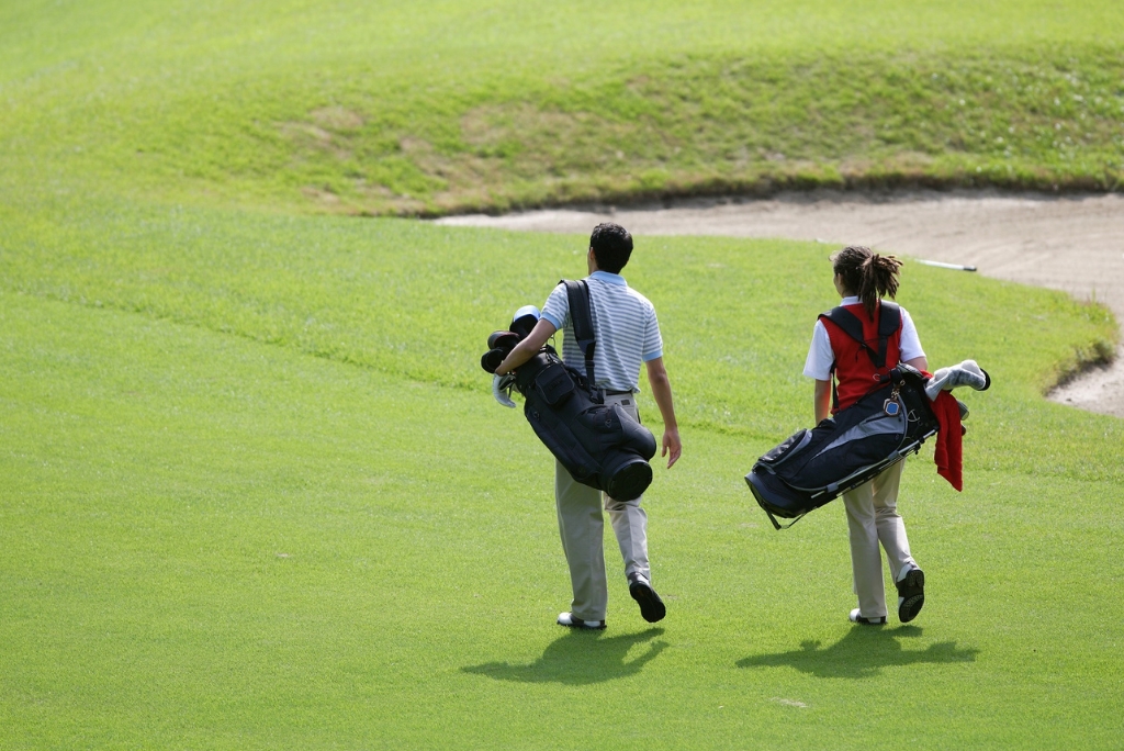 Student golfers carrying clubs on a course, representing college golf recruiting.