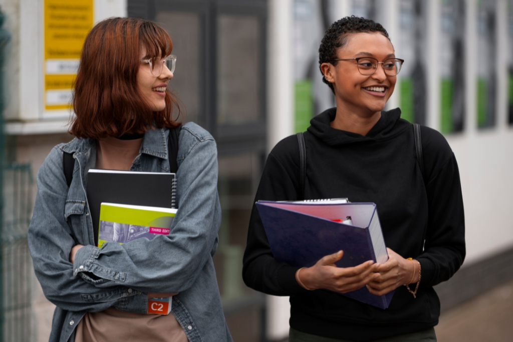 Two college students holding notebooks while walking together on campus.