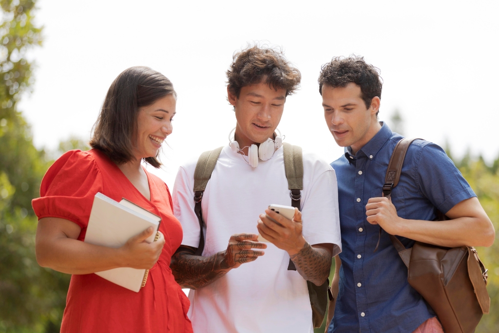 College students reviewing information on a phone while discussing admissions planning on campus.