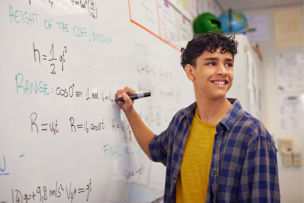 High school student solving physics equations on a whiteboard during STEM academic preparation.