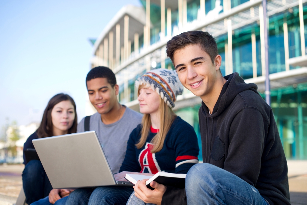 High school students using a laptop and notes while preparing for college admissions.